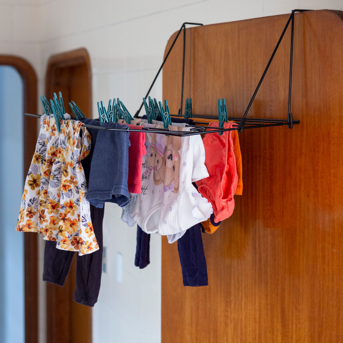 Roupinha de bebê colorida secando em varal suspenso, com bodies, calças e blusas estampadas, ideal para organização prática e moderna.